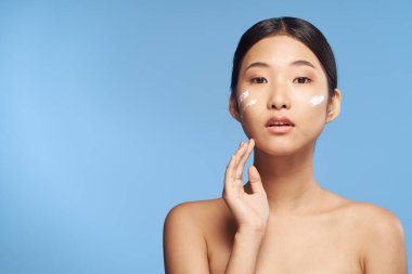 Stüdyoda mavi arka planda krem sürmüş genç Asyalı kadın. 