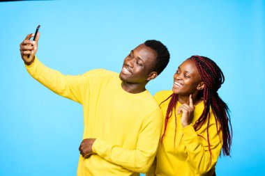 Genç ve güzel bir çift stüdyoda mavi arka planda selfie çekiyor.