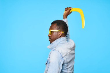 Bumeranglı genç Afrikalı adam mavi arka planda izole edilmiş.