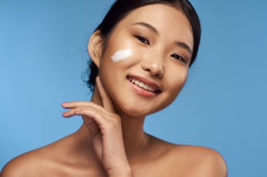 Genç Asyalı kadın yüzüne nemlendirici sürüyor. 