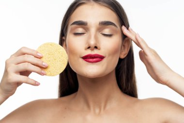 Genç ve güzel bir kadın yüzünü süngerle temizliyor. Güzellik rutini. Stüdyo çekimi