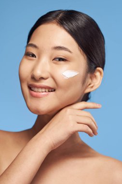 Stüdyoda mavi arka planda gülümseyen genç Asyalı kadın. 