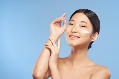 Güzel Asyalı bir kadının portresi izole edilmiş arka planda krem sürüyor.