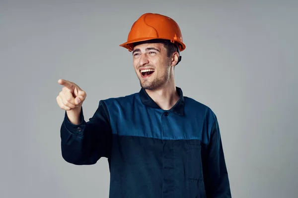 Studio shot. Young worker in orange helmet pointing