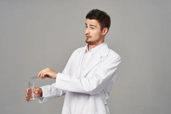 confused Doctor in lab coat with test tubes on grey background. Studio shot