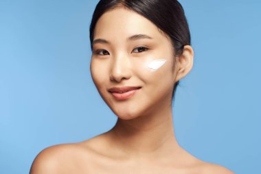 Güzel Asyalı bir kadının portresi izole edilmiş arka planda krem sürüyor.