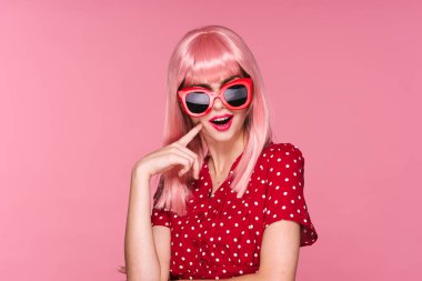 Pembe peruklu genç kadın pembe arka planda güneş gözlüğü takıyor.