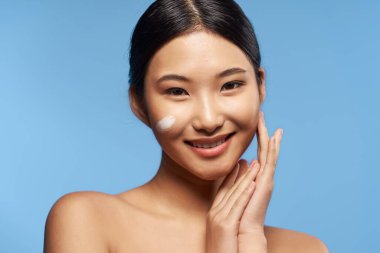 Genç Asyalı kadın yüzüne nemlendirici sürüyor. 