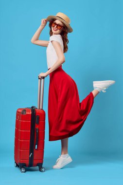 Stüdyoda kırmızı valizli genç bir kadın var.