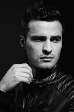 Stüdyoda poz veren siyah deri ceketli yakışıklı bir adamın portresi. Siyah ve beyaz  