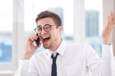 Ofiste akıllı telefondan konuşan mutlu bir iş adamı. 