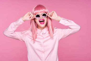 Pembe peruklu ve güneş gözlüklü genç bir kadın stüdyoda poz veriyor. 