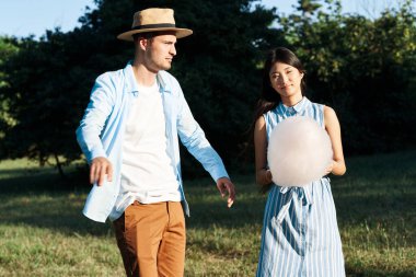 Genç bir çift ellerinde pamuk şekerle parkta yürüyor. 