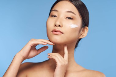 Genç Asyalı kadın yüzüne nemlendirici sürüyor. 