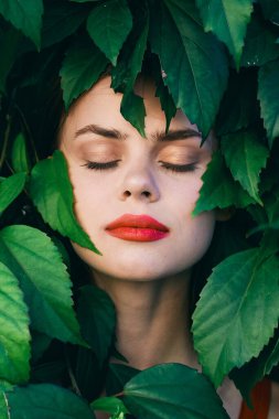 Yüzünde yapraklarla poz veren genç ve güzel bir kadın.