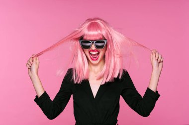 Pembe peruklu ve güneş gözlüklü genç bir kadın stüdyoda poz veriyor. 