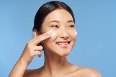 Genç Asyalı kadın yüzüne nemlendirici sürüyor. 
