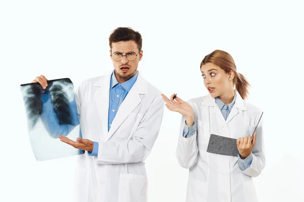 Studio shot. Young angry  doctor  with x-ray and nurse on isolated background