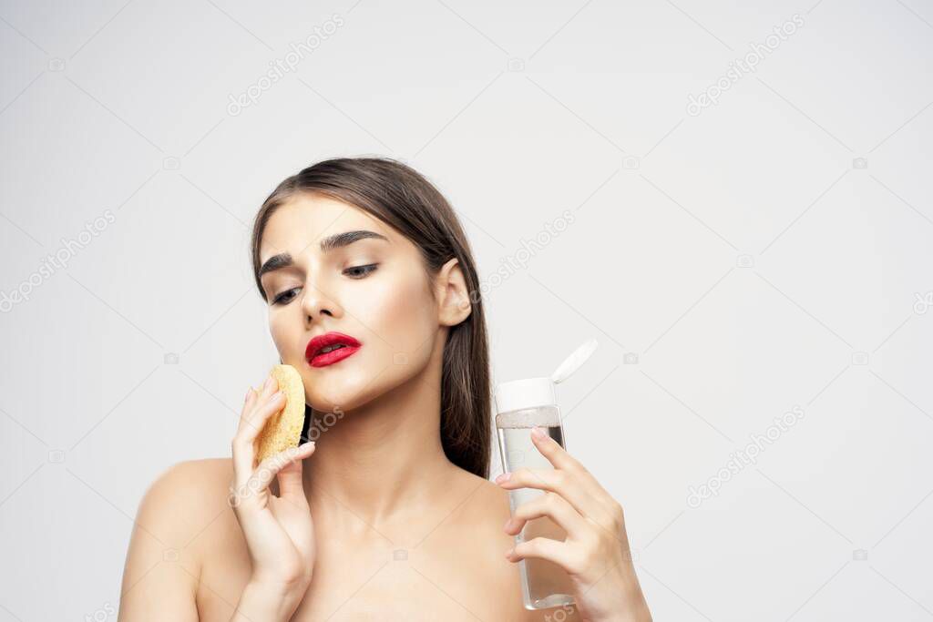 Young beautiful woman cleaning her face with sponge. Beauty routine. Studio shot