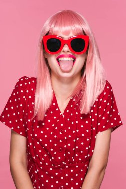 Pembe peruklu genç kadın pembe arka planda dilini gösteriyor.