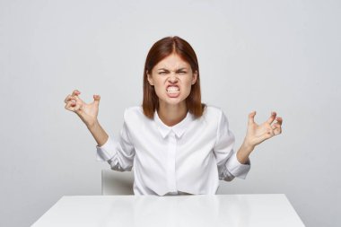 Stüdyo çekimi. Genç kızgın iş kadını masada oturmuş bağırıyor.