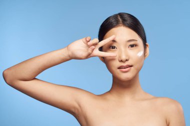 Genç Asyalı kadın yüzüne nemlendirici sürüyor. 