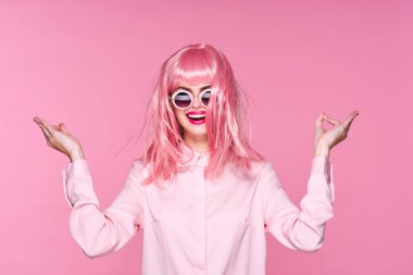 Pembe peruklu ve güneş gözlüklü genç bir kadın stüdyoda poz veriyor. 