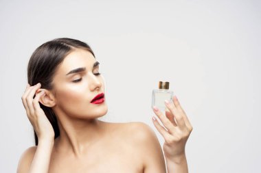 Stüdyoda gözleri kapalı, parfüm şişesi tutan genç ve güzel bir kadın.