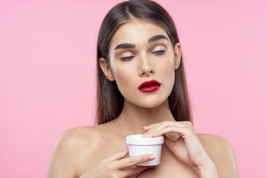Güzel bir kadının portresi pembe arka planda güzellik ürünü taşıyor.