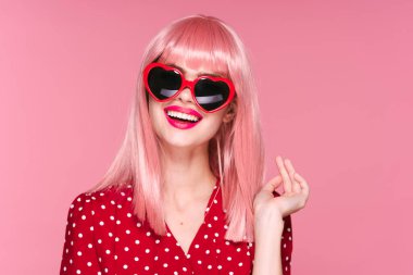Pembe peruklu ve güneş gözlüklü genç bir kadın stüdyoda poz veriyor. 