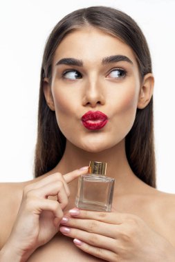 Stüdyoda kırmızı dudaklı güzel bir kadın parfüm şişesi tutuyor.
