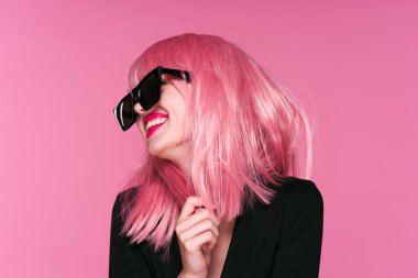 Pembe peruklu ve güneş gözlüklü genç bir kadın stüdyoda poz veriyor. 