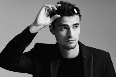 Stüdyoda güneş gözlüğü takan yakışıklı genç adam, siyah ve beyaz. 