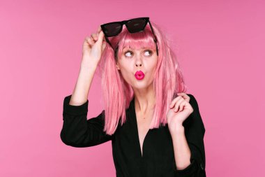 Pembe peruklu ve güneş gözlüklü genç bir kadın stüdyoda poz veriyor. 