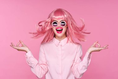 Pembe peruklu ve pembe arka planda güneş gözlüklü genç bir kadın.