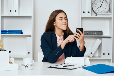 İş kadını elinde hesap makinesiyle ofiste oturuyor. 