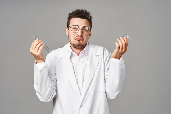 confused Doctor in lab coat with test tubes on grey background. Studio shot