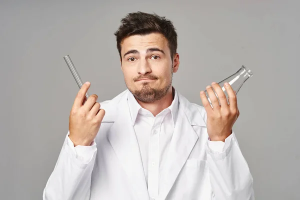 Young confused  doctor in lab coat with test tubes on grey background