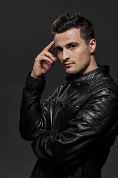 Young handsome man in leather jacket posing in studio on dark background