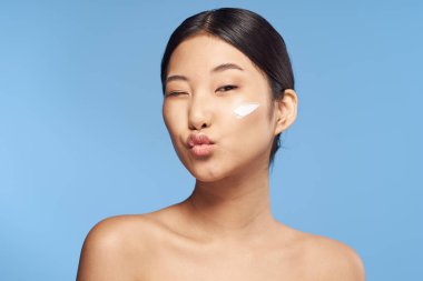 Genç Asyalı kadın yüzüne nemlendirici sürüyor. 