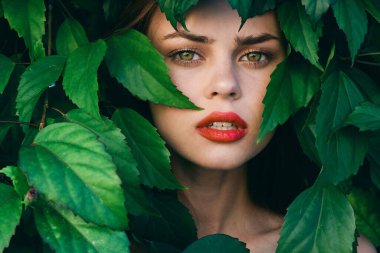 Yüzünde yapraklarla poz veren genç ve güzel bir kadın.