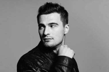 Stüdyoda poz veren siyah deri ceketli yakışıklı bir adamın portresi. Siyah ve beyaz  