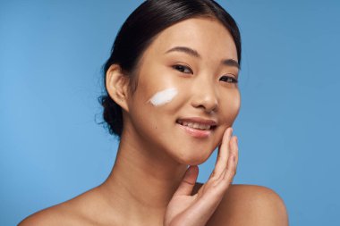 Genç Asyalı kadın yüzüne nemlendirici sürüyor. 