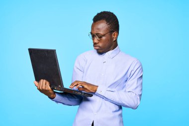 Dizüstü bilgisayarı tutan genç Afrikalı iş adamı mavi arka planda izole edildi