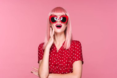Pembe peruklu ve güneş gözlüklü genç bir kadın stüdyoda poz veriyor. 