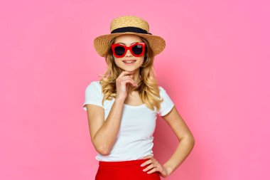 Stüdyoda pembe arka planda şapka ve güneş gözlüğü takan kadın.      