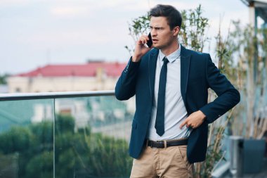 Genç kızgın iş adamı sokakta akıllı telefondan konuşuyor. 