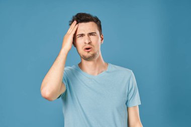 Genç yakışıklı adamın mavi arka plandaki stüdyoda kafası karışmış. 