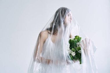 Plastik çarşafın altında elinde çiçekler olan genç bir kadın. Ekoloji kavramı