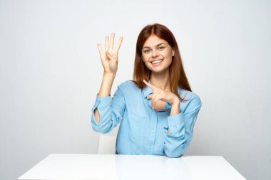 Genç ve güzel bir iş kadını ofiste oturuyor ve sana parmaklarını gösteriyor. 